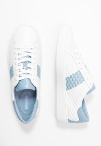 Białe trampki z jasnoniebieskimi akcentami, teksturowane boczne panele, gładkie wykończenie ze skóry, okrągły nosek i kontrastująca niebieska zakładka na pięcie.