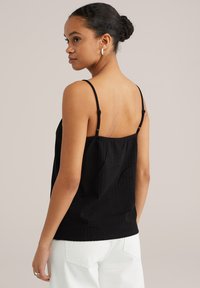 Top nero in satin con spalline sottili regolabili e tessuto strutturato. La parte posteriore presenta un design arricciato, indossato con jeans bianchi a vita alta.
