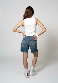 Hvid ærmeløs top med lyserøde bølgekant, parret med højhalsede denimshorts. Båret med hvide sneakers og sokker.