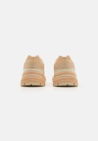 Beige athletic shoes with reflective stripes, cushioned soles, and a textured finish. Features a soft upper and branded detailing.