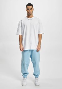 Tricou alb oversized, pantaloni scurți albaștri deschiși și adidași albi cu o talpă texturată. Design simplu, croială lejeră și material neted.