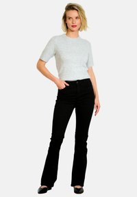 Suéter corto de manga corta en gris claro, diseñado ajustado, combinado con jeans negros de campana. Textura suave, estilo casual, diseño minimalista, silueta simple.