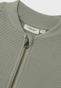 Svetlošedá pletená detská bunda s textúrou, s kovovým zipsom a rebrovaným golierom, označená veľkosťou 1½-2 roky od značky Lil' Atelier.