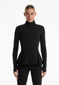 Zwarte ritsjack met lange mouwen en hoge kraag. Voorzien van een uitlopende peplum taille en duimgaten bij de mouwmanchetten. Gladde textuur.
