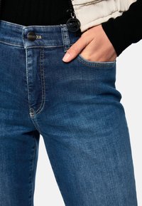 Blaue Jeans aus Denim mit schmaler Passform, ausgestattet mit einer Fronttasche, Metallknopfverschluss und dezenten Nahtdetails an den Nähten.