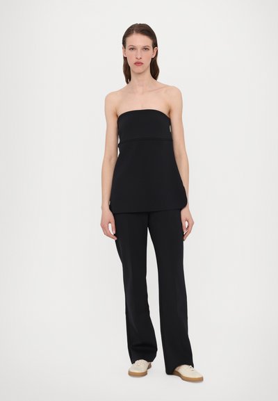 Svart strapless topp med en tettsittende korse og utsvungen kant, kombinert med svarte vide bukser. Skoene er beige med lyse brune såler.