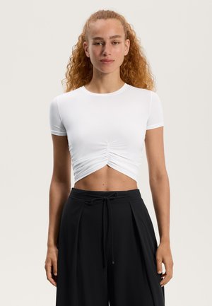 Witte cropped t-shirt met korte mouwen en een geraffineerd ontwerp aan de voorkant. Gecombineerd met zwart hoge taille broek met een trekkoord in de taille.