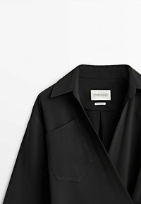 Musta kauluspaita, jossa on tasku ja sileä kangas. Mukana on etiketti, johon on kirjoitettu "Massimo Dutti Limited Edition".