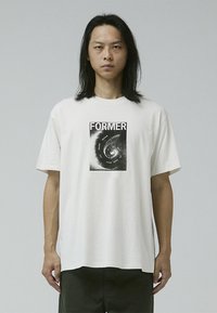 White cotton t-shirt featuring a black graphic print of the word "FORMER" and swirling design, with a relaxed fit and short sleeves.