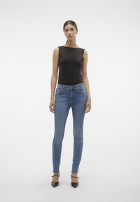 Top negro sin mangas, jeans skiny de mezclilla azul y tacones negros puntiagudos. Diseño simple, textura suave y silueta ajustada.