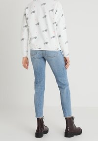 Camisa blanca de manga larga con estampado de animales en negro, combinada con jeans de mezclilla azul claro y botas de tobillo negras con cordones.