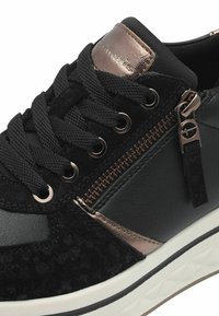 Svart sneaker med en texturerad ovandel i mocka och läder. Har bronserade detaljer, svarta snören och en sidodragkedja för extra detalj.