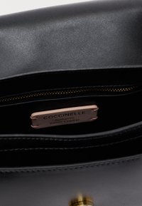 Interieur van een zwarte leren handtas met een gladde textuur, gouden ritssluiting en een zichtbaar label met de tekst "Coccinelle, Authentiek Italiaans Leer."