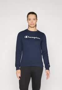 Sweatshirt bleu marine avec poignets et ourlet côtelés, portant le logo "Champion" blanc sur la poitrine. Tissu en mélange de coton, design à col rond.