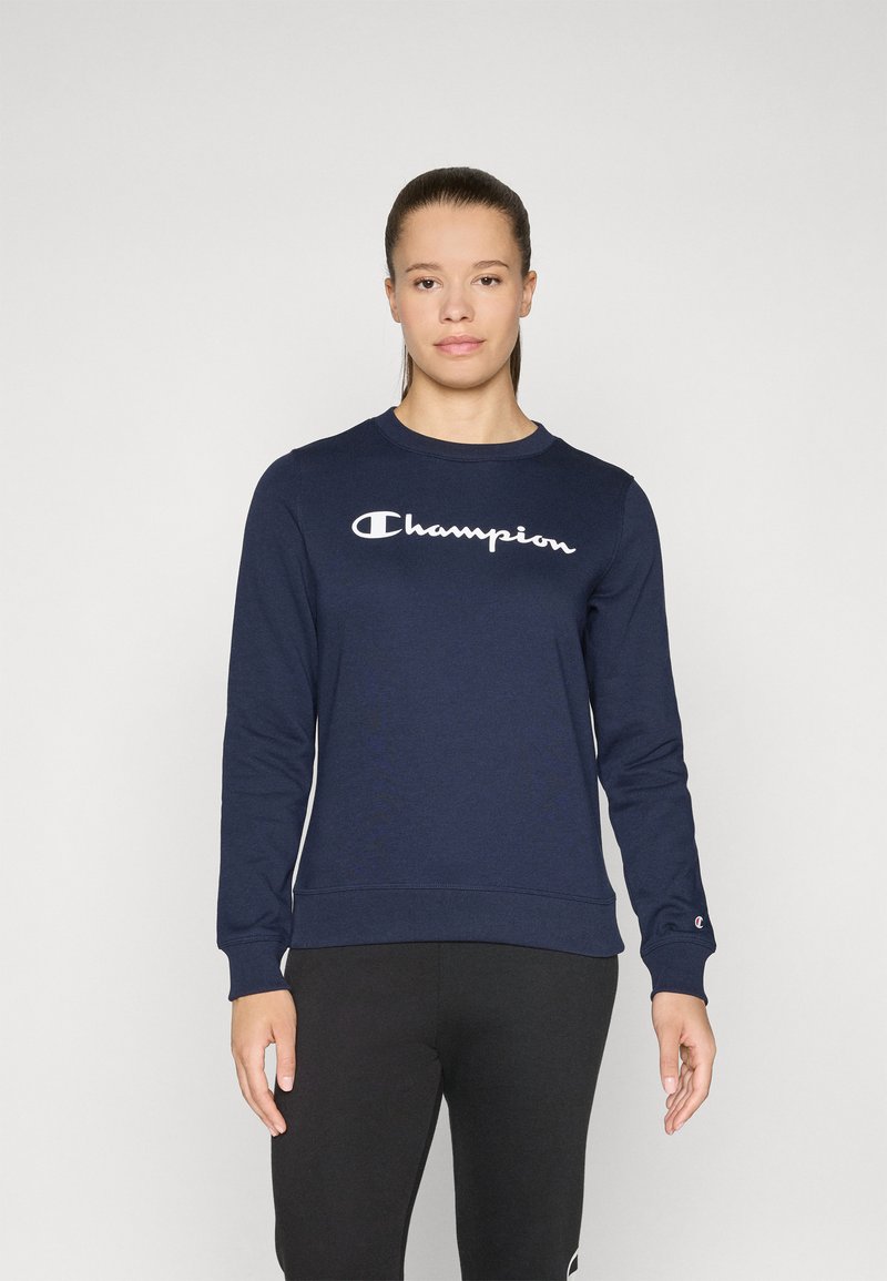 Sweatshirt bleu marine avec poignets et ourlet côtelés, portant le logo "Champion" blanc sur la poitrine. Tissu en mélange de coton, design à col rond.