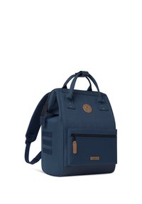 Zaino blu navy dalla forma rettangolare, realizzato in tessuto resistente, con una tasca frontale con zipper e un'etichetta in pelle.