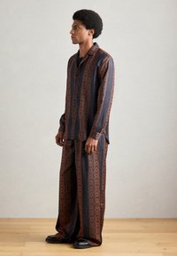 Conjunto de dos piezas con estampado en azul marino y naranja. La camisa presenta un diseño geométrico; los pantalones son de pierna ancha y están hechos de un tejido sedoso.