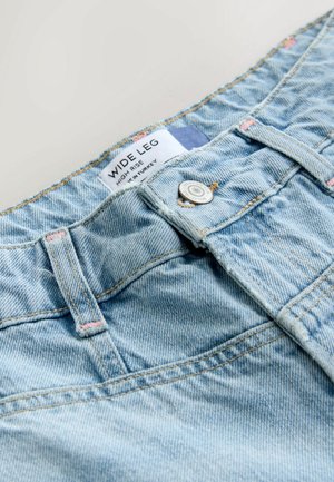 Heledad sinine laiapõhjaline denim püksid, millel on kõrge vöökoht, hõbedane nööbilukk ja kontrastne kollane õmblus. Silt on nähtav.