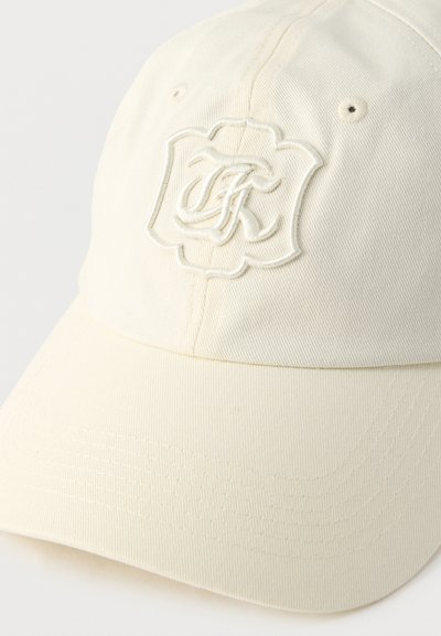 Lippalakki off-white-värisestä puuvillasta, jossa jäsennelty muotoilu. Siinä on kirjailtu logoyksityiskohta, kaareva lippa ja saumat reunoilla.