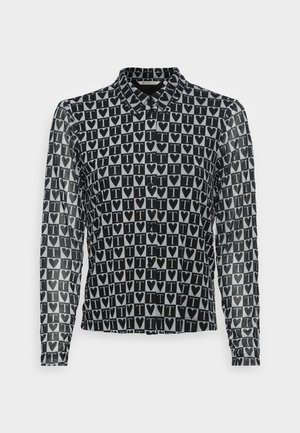 Chemise à manches longues noir et blanc avec un motif répétitif de cœurs noirs et la lettre T à l’intérieur de carrés blancs, boutonnée sur le devant avec col.