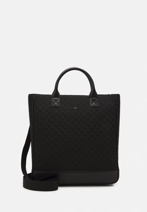 Zwarte gewatteerde boodschappentas met leren handvatten en schouderriem, met een slank rechthoekig ontwerp en een geperst merklogo in het midden aan de voorkant.