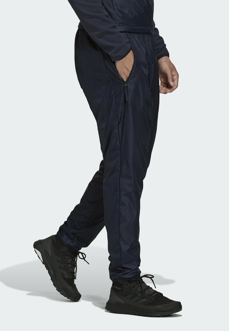 Pantalones ligeros de color marino con bolsillos con cremallera, cintura elástica, piernas ajustadas y una textura suave. Combinados con zapatillas deportivas negras.