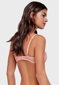 Soutien-gorge rose pâle avec panneaux en mesh, bretelles ajustables et fermeture à crochets. Texture lisse avec des accents à pois au dos. Design simple.