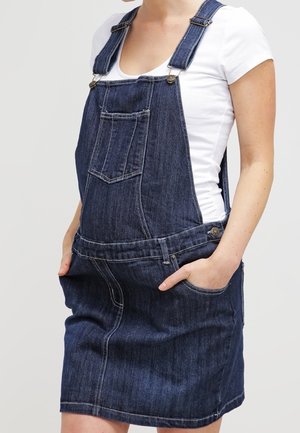 Sukienka ogrodniczka z denimu z regulowanymi ramiączkami, przednią kieszenią i kieszeniami po bokach. Ciemnoniebieski kolor z jasnym przeszyciem i dopasowanym fasonem.