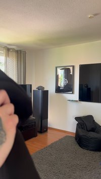 Fekete babzsák szék egy világos fahalon, szürke szőnyeg, sötét TV-szekrény, lapos képernyős TV, és egy keretezett tükör, amely visszatükrözi a szobát.