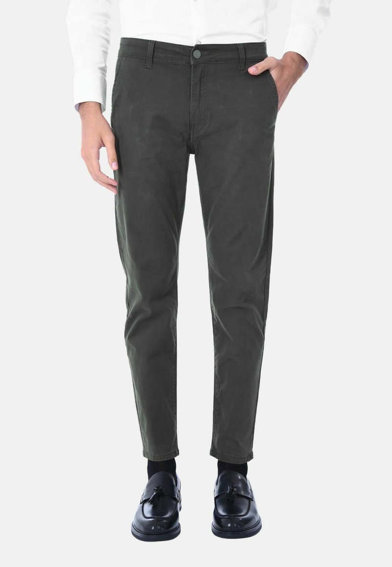 Chino affusolati verde scuro con una texture liscia, dotati di chiusura a bottone, tasche laterali e orli cuffi, abbinati a scarpe nere.