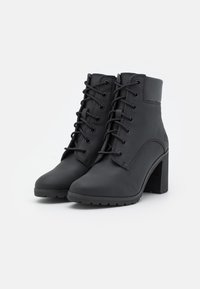 Černé kožené kotníkové boty s šněrováním v přední části, vysokým blokovým podpatkem a texturovanou podrážkou. Hladký povrch s minimálními akcenty, stylový design.