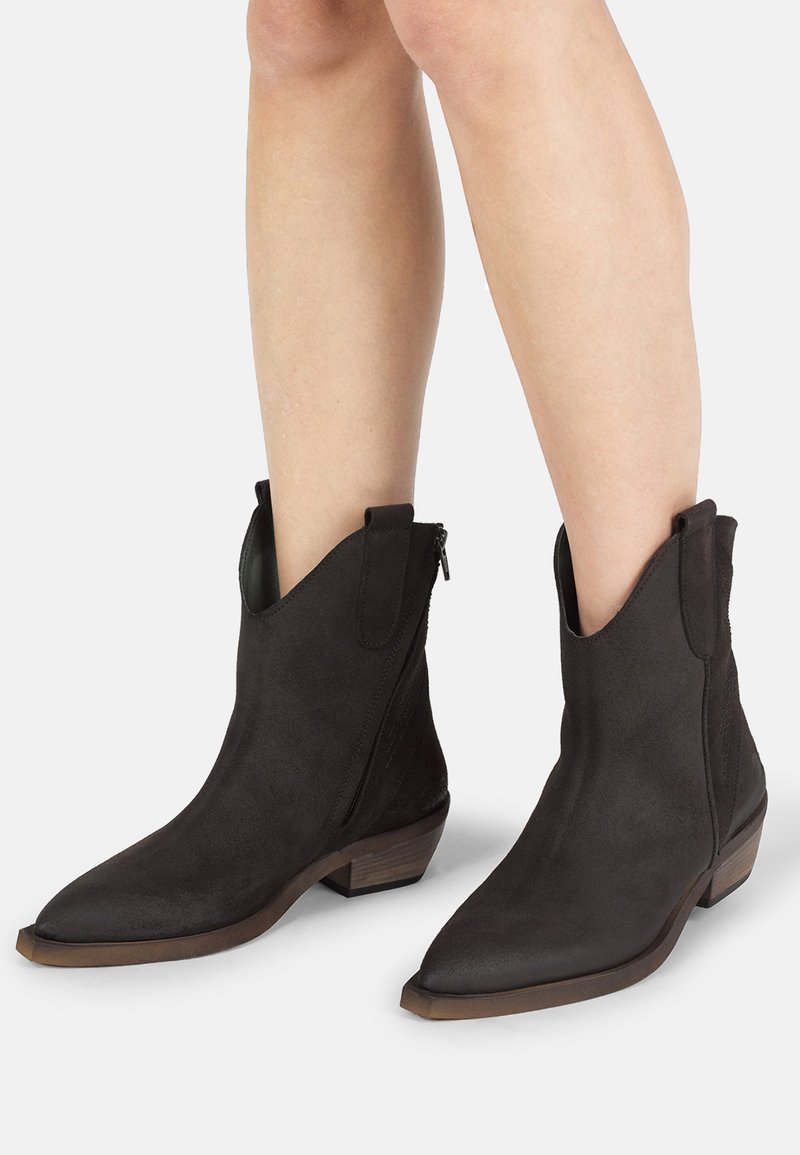 Stivali ankle in suede nero con punta appuntita, zip laterale e tacco corto a blocco. Presentano dettagli a taglio al colletto.