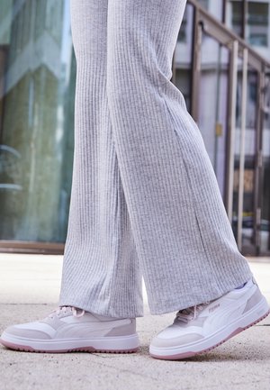 Vita och ljusgrå sportskor med rosa accenter, texturerad design, mjuka material och låg profil. Bärs med ljusgrå ribbade byxor.