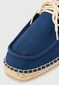 Espadrille slip-on en toile bleue tissée, présentant un dessus texturé, des lacets beiges et une semelle en jute naturel avec une finition tressée.