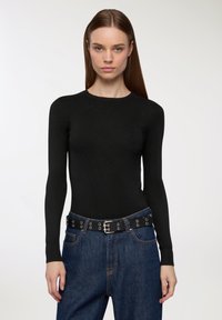 Czarna dopasowana bluzka z długim rękawem i okrągłym dekoltem, połączona z dżinsami z wysokim stanem i czarnym paskiem z srebrnymi akcentami.