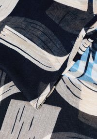 Námořnická tkanina s abstraktními světle béžovými a modrými vzory. Hladká textura s různými tahy štětcem a přehnutým rohem.