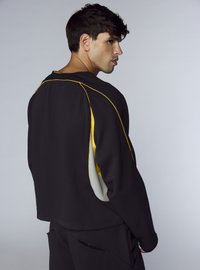 Felpa nera con accenti gialli e grigi, caratterizzata da una vestibilità rilassata e dettagli di cuciture visibili, vista da dietro.