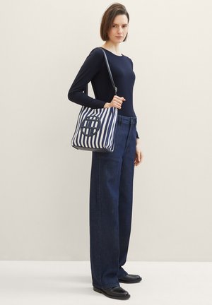 Sac à épaule en toile rayée bleu marine et blanc, avec un détail en forme de découpe circulaire, une forme structurée et une bandoulière réglable.