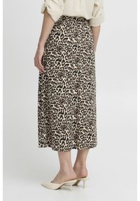 Leopardmuster-Midirock mit glatter Textur, ausgestattet mit einem dunkelbraunen und beigen Muster. Kombiniert mit beigen High-Heel-Mules.