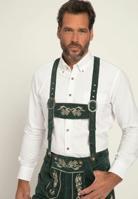 Grønne ruskind lederhosen med broderede blomsterdesigns, sølv hardware og en hvid skjorte med krave og knapper. Struktureret stof.