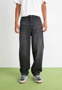 Løse svarte denimjeans har høy midje, rette ben og subtil fading. Kombinert med grå joggesko og en hvit T-skjorte.