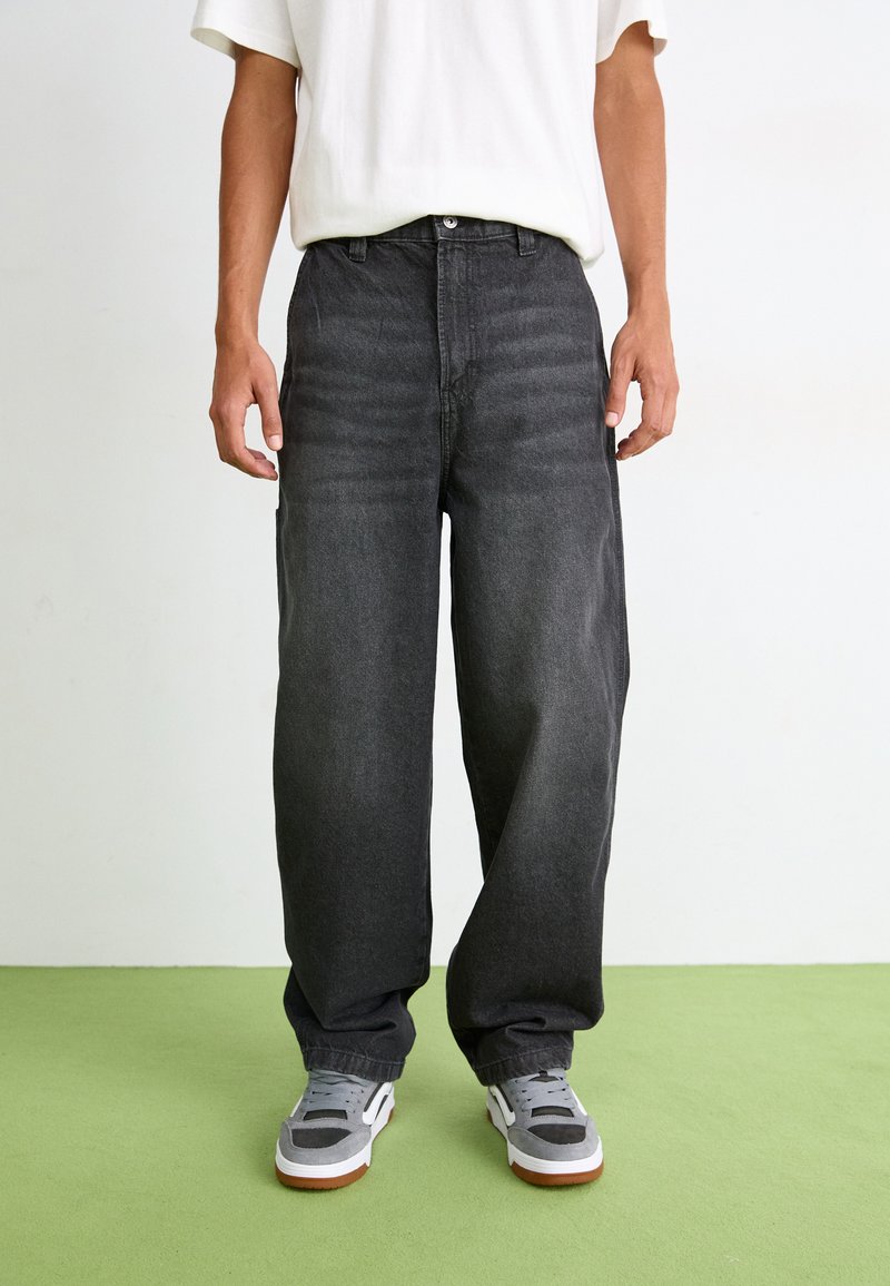 Løse svarte denimjeans har høy midje, rette ben og subtil fading. Kombinert med grå joggesko og en hvit T-skjorte.