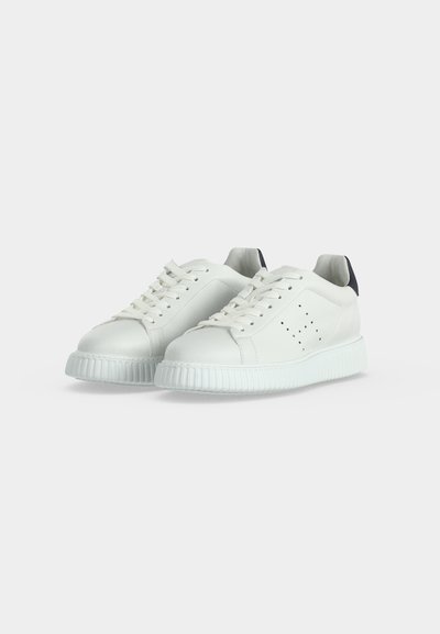 Paire de baskets blanches basses avec lacets à l'avant, détails perforés sur les côtés et languettes foncées au talon sur un fond clair uni.