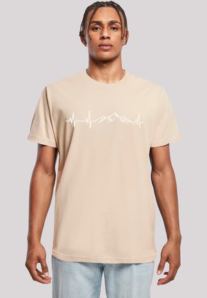 Beige cotton t-shirt with short sleeves, featuring a white heartbeat line and mountains graphic across the chest. Classic crew neck design.