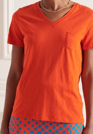 Orange cotton t-shirt with a v-neck, short sleeves, and a left chest pocket, paired with patterned blue skirt featuring dots.