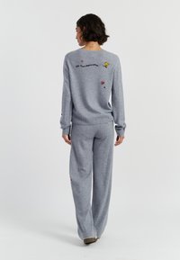Grijze gebreide lounge set met een langefsleevetop met geborduurde details en bijpassende wijde broekspijpen, zachte textuur en ontspannen pasvorm.