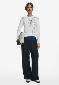 Maglione bianco con disegni floreali in rosa, blu e giallo; abbinato a pantaloni largo blu navy e calzature bianco e nere. Incluso anche una borsa grigia.