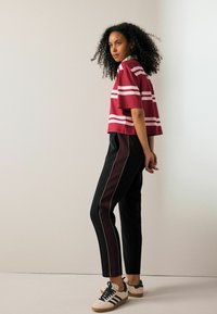 Bordeaux stribet cropped top parret med sorte og burgunder bukser med sidestriber. Fodtøj er en beige sneaker med teal detaljer.