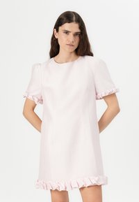 Vestido rosa claro com um tecido texturizado, mangas curtas em balão com punhos franzidos e uma bainha com babados. Silhueta simples e reta.