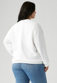 Felpa bianca in un materiale morbido con una vestibilità rilassata, caratterizzata da maniche lunghe e scollatura arrotondata. Abbinata a jeans in denim blu.